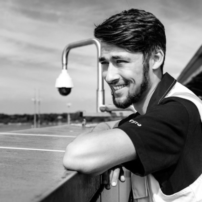 Schwarz-weiß-Fotografie vom OpteMe Geschäftsführer Leon Kruse im Freien, der sich an ein Geländer lehnt