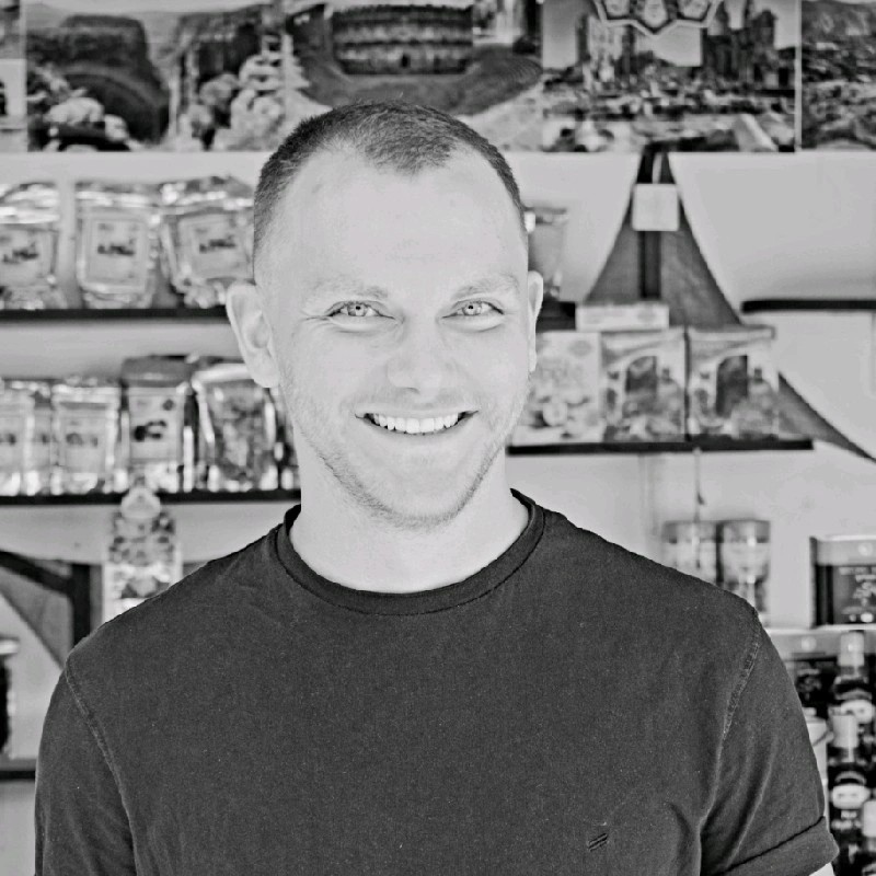 Schwarz-weiß-Porträt vom OpteMe Geschäftsführer Felix Heiden, der vor einem Regal mit Produkten steht