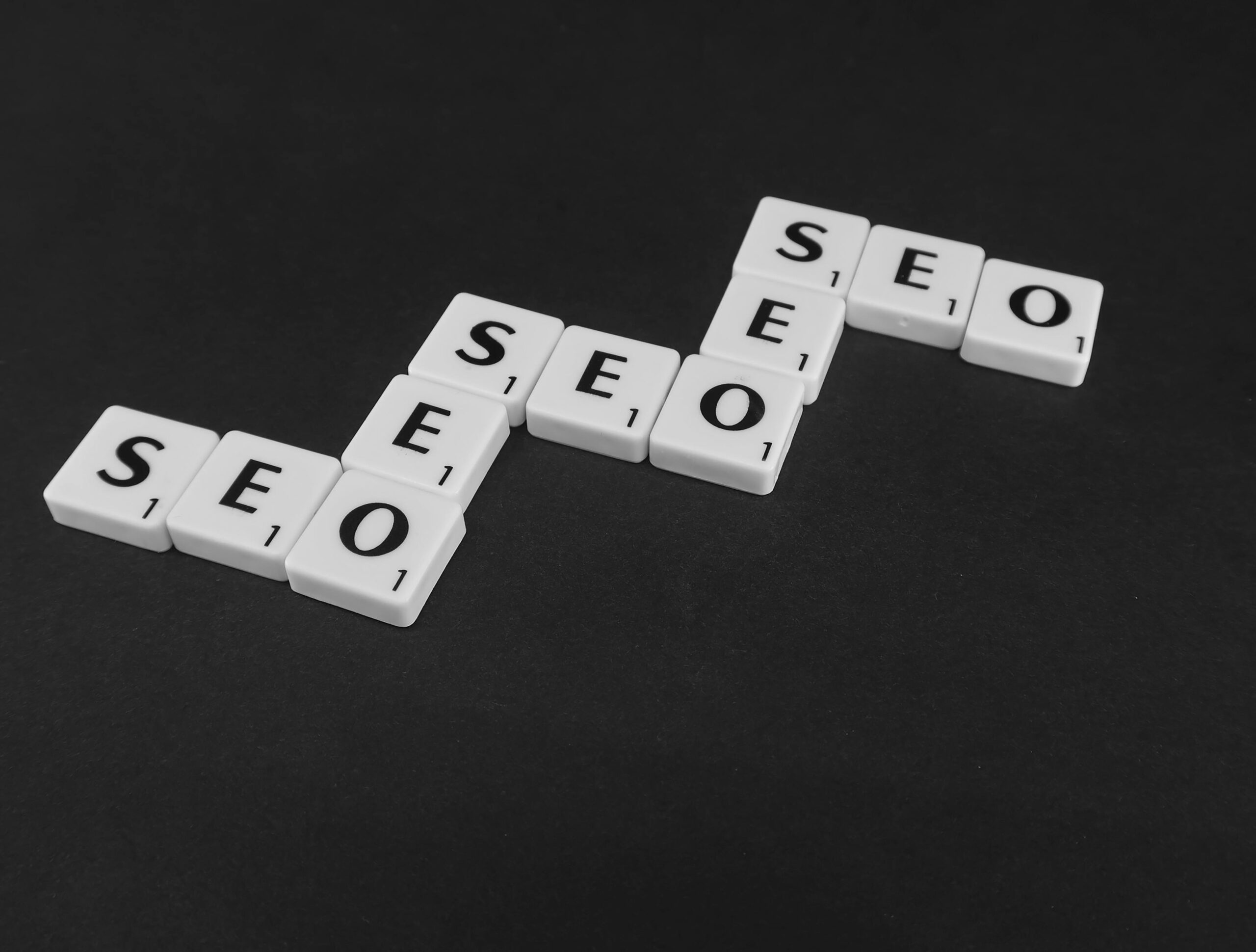 Mehrere weiße Buchstabenplättchen mit der Aufschrift SEO liegen auf schwarzem Hintergrund