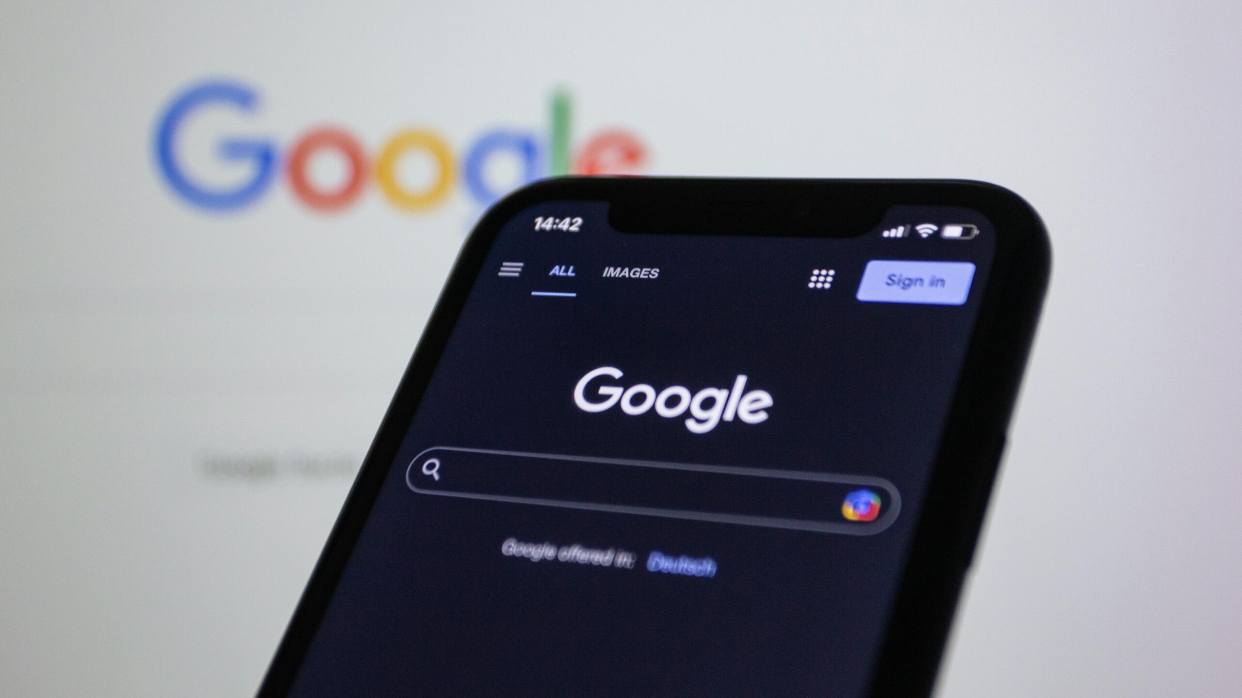 „Smartphone mit geöffneter Google-Suchseite im Dunkelmodus, unscharf im Hintergrund das Google-Logo – Symbol für Online-Suche und Suchmaschinenoptimierung.“